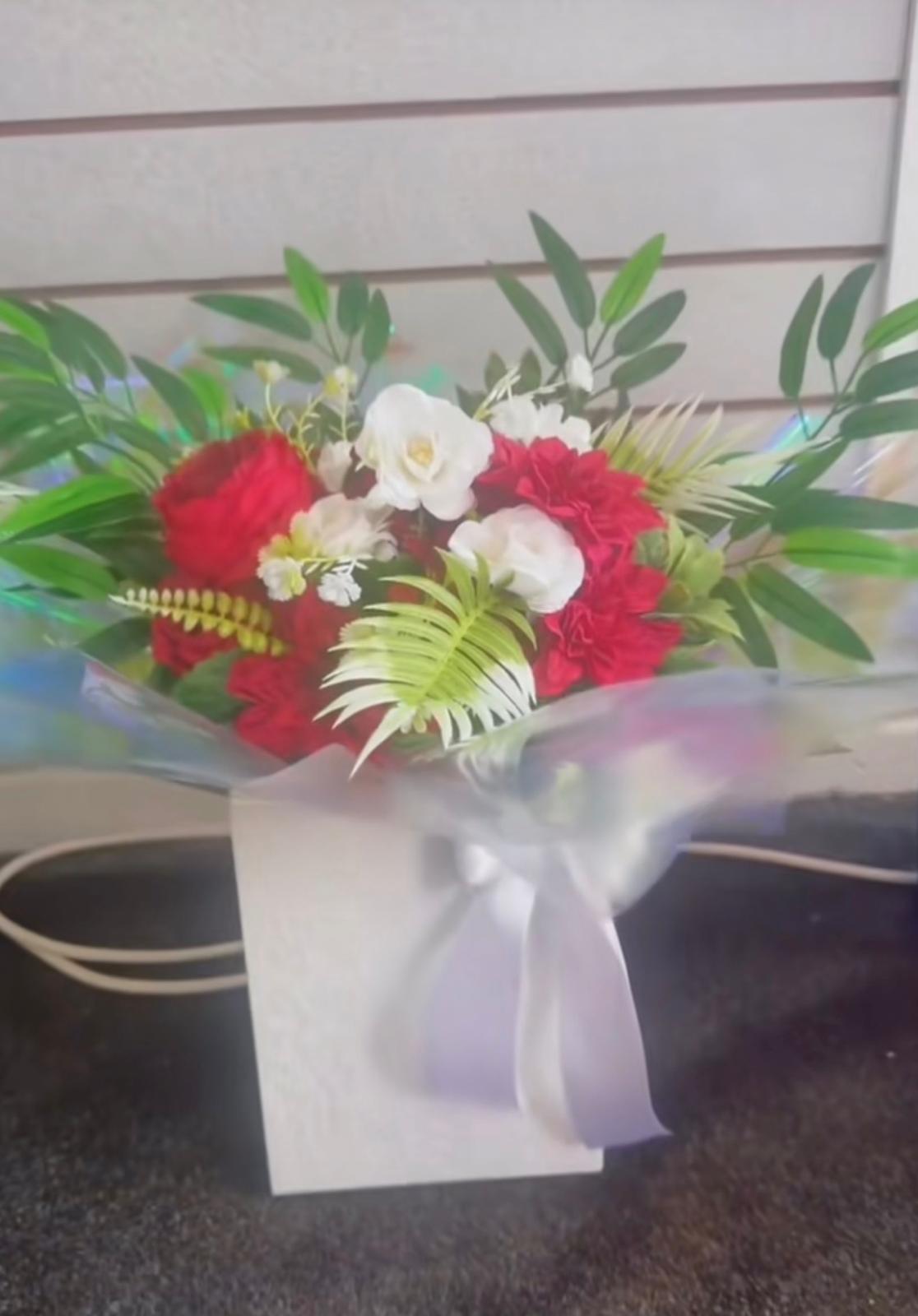 Red carnations and white roses with green foliage in a white gift box