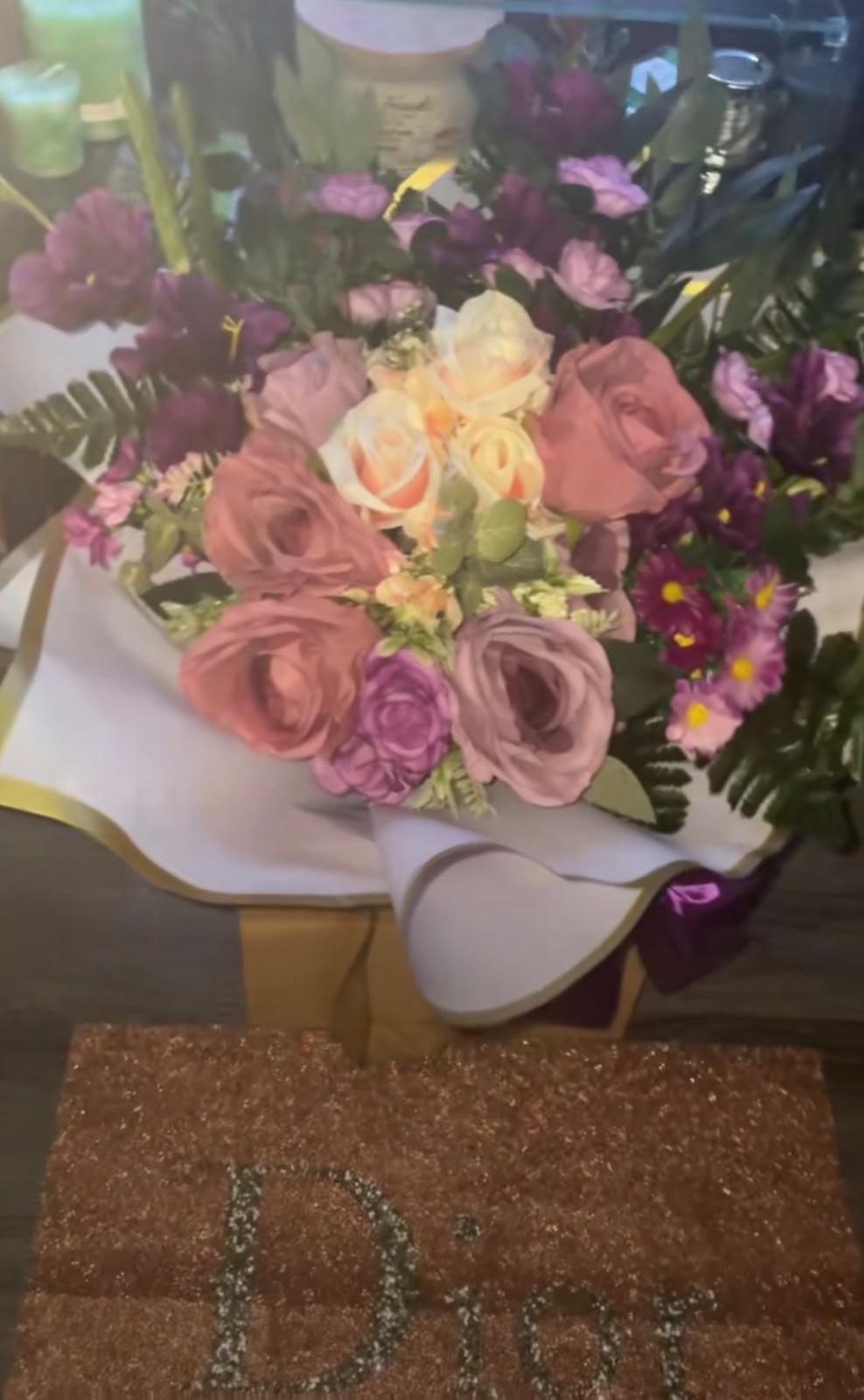 Artificial bouquet of dusky pink roses, plum blooms and purple daisies in white wrap