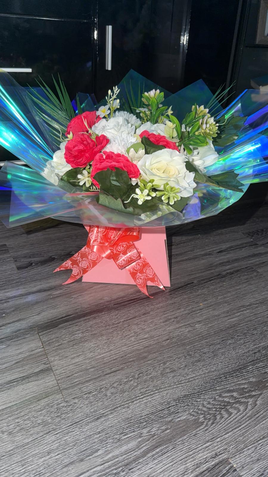 Red carnations with ivory roses and chrysanthemums in iridescent wrap on a pink gift box