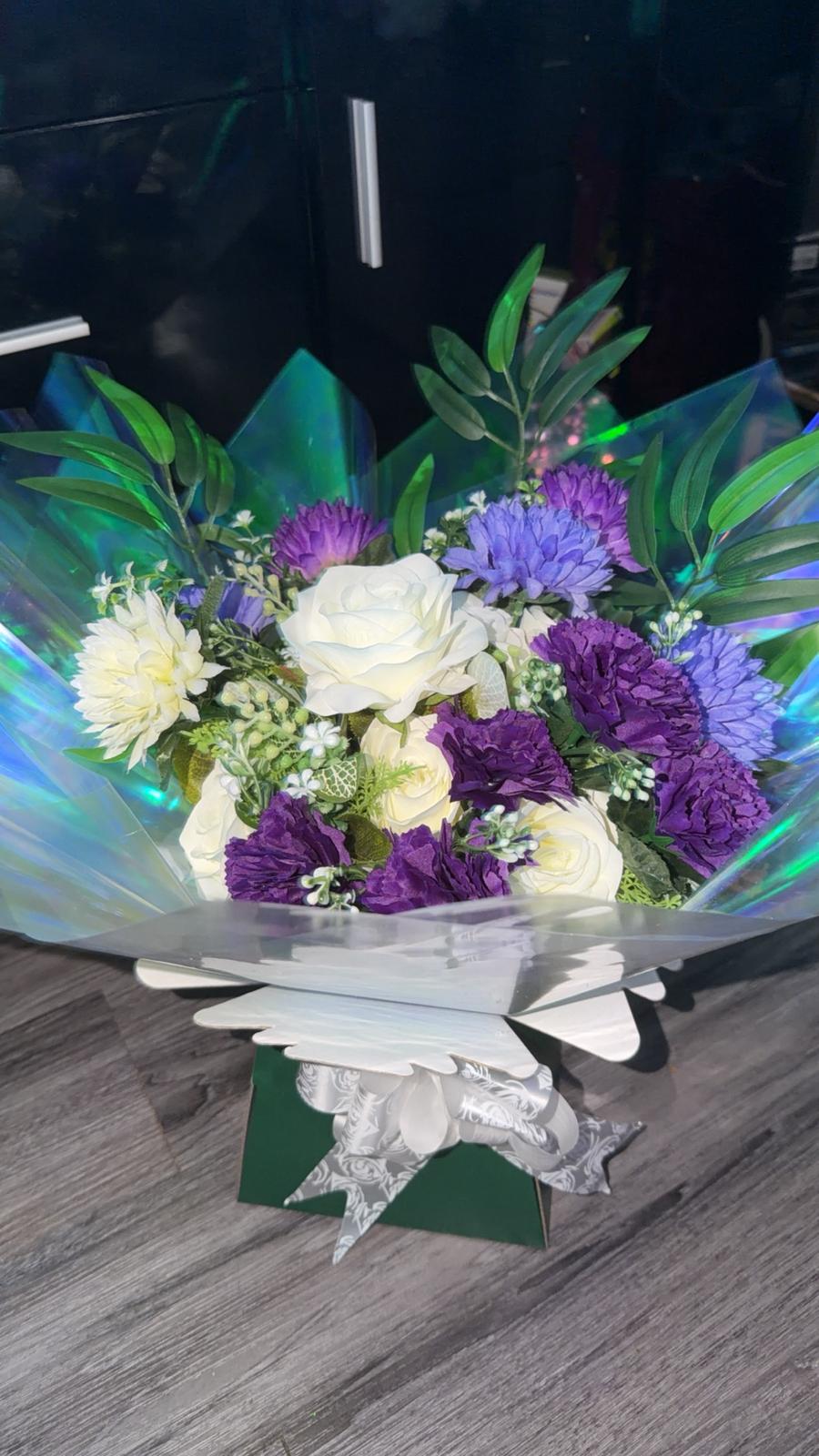 Purple and lilac carnations and chrysanthemums with white roses and olive foliage in a green gift box