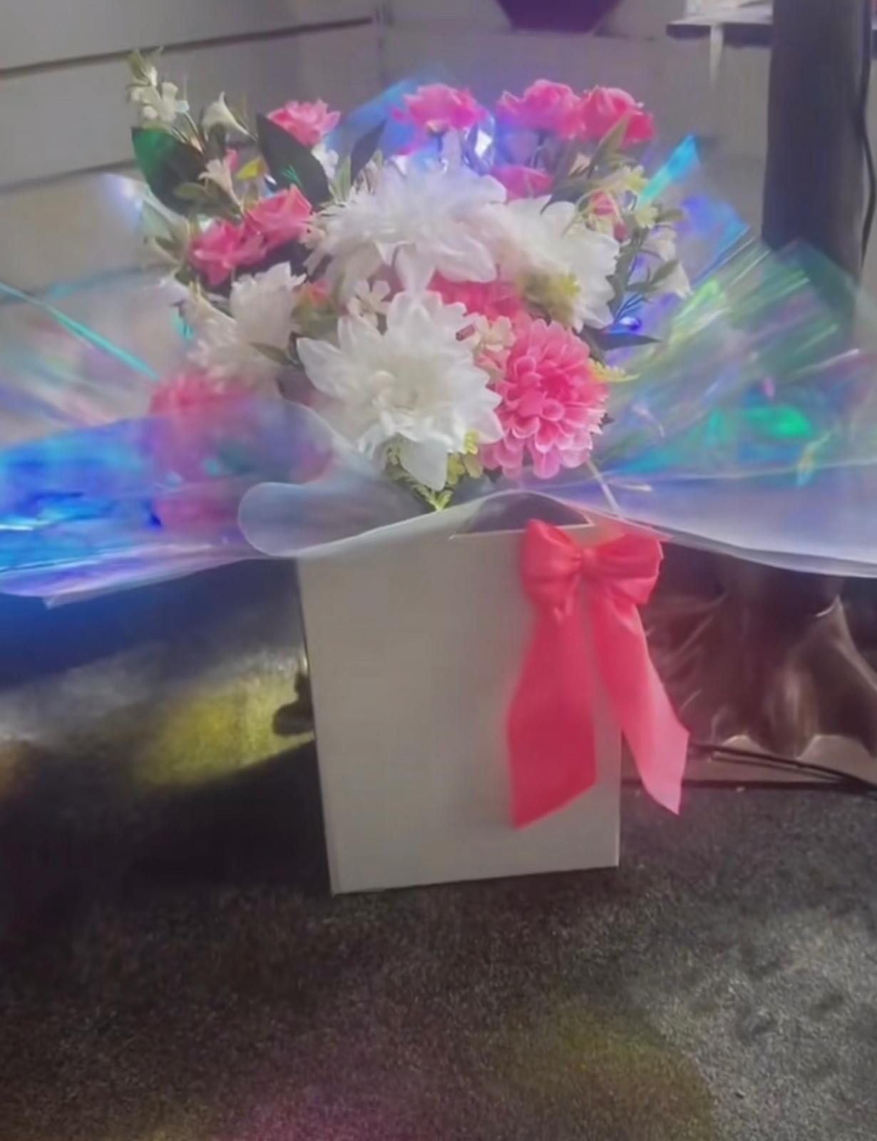 Pink and white artificial arrangement in a white box with iridescent wrap and red bow