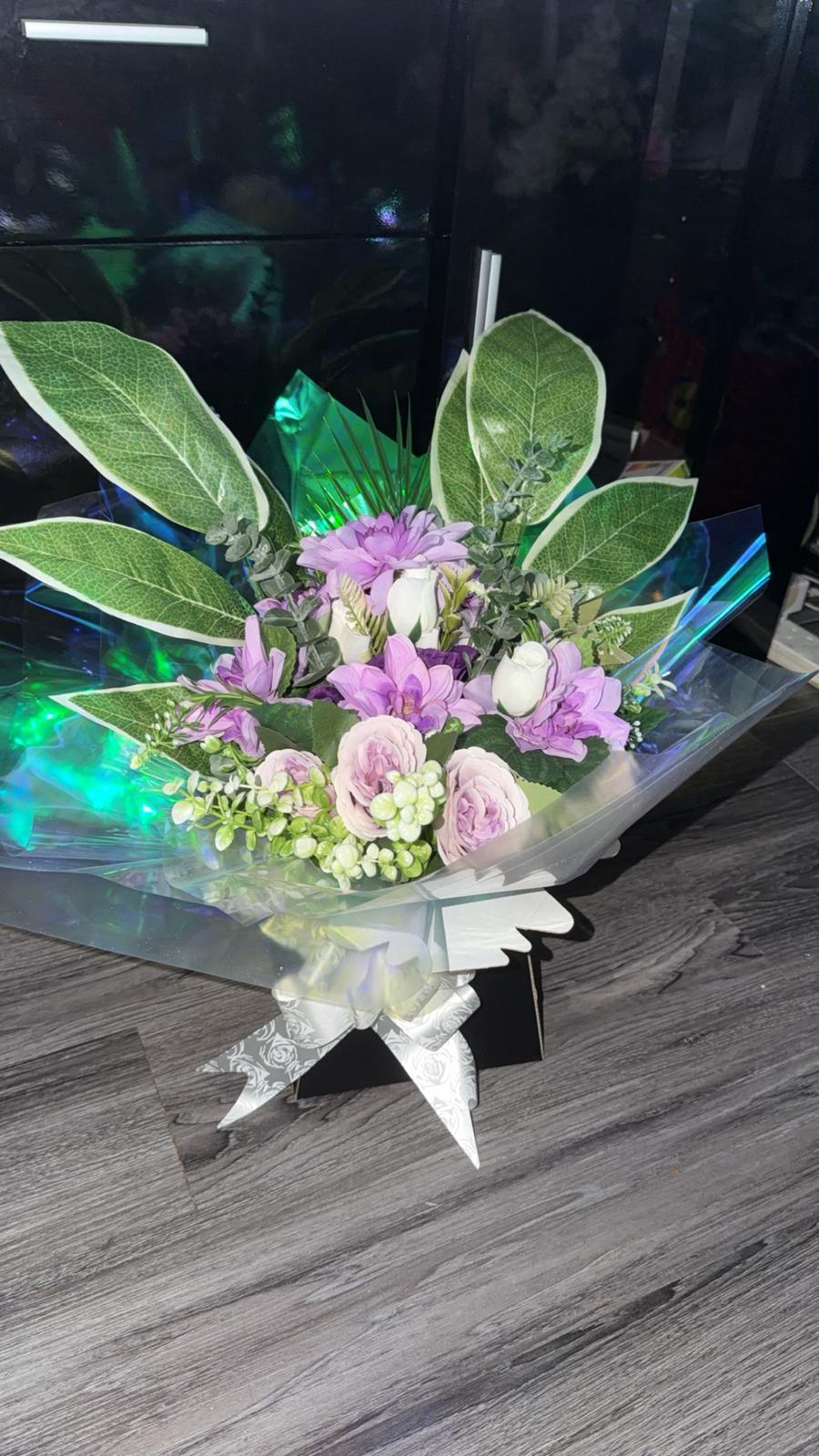 Lilac freesia and roses with white buds, berries and large variegated leaves in a black gift box