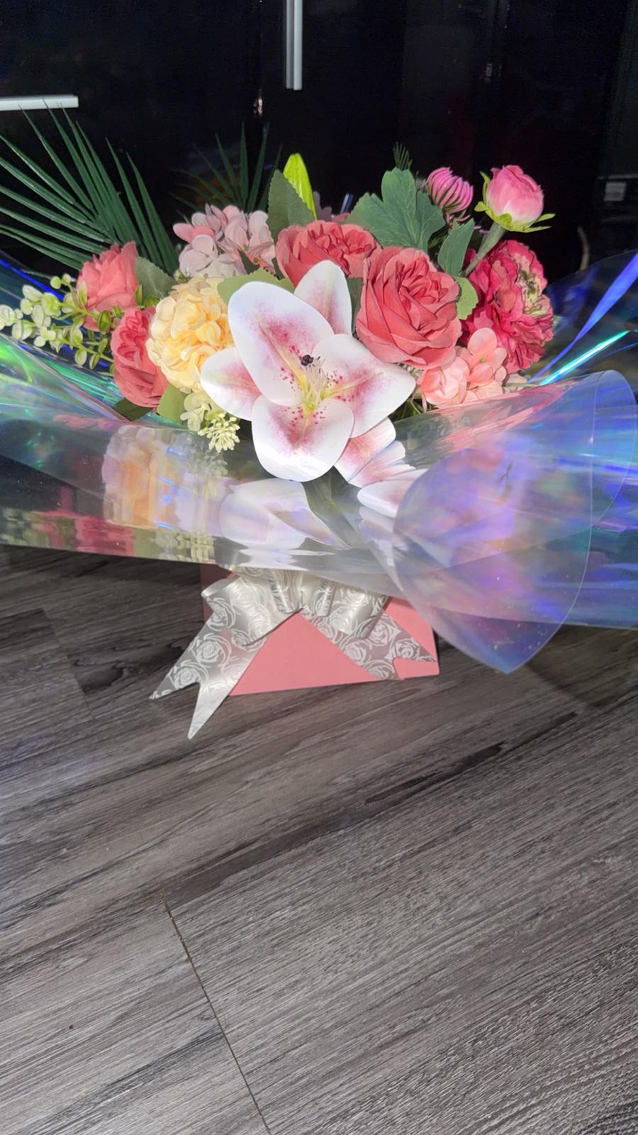 Coral roses, peach hydrangea and a pink-freckled lily in an iridescent wrapped gift box